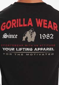 Zwarte katoenen t-shirt met rode en witte tekst: "GORILLA WEAR," "Sinds 1982," en "JOUW LIFTKLEDING," met een gorilla-illustratie.