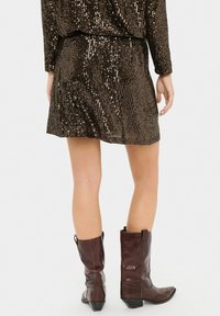Vestido mini marrón con lentejuelas, ajuste ceñido en la cintura, mangas largas y un dobladillo corto. Combinado con botas de vaquero marrones con tacón, con punta afilada.