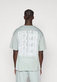 Ανοιχτό πράσινο υπερμεγέθες t-shirt με λευκή γραφική επιγραφή στην πλάτη που γράφει «PICK IT UP, PUT IT DOWN». Απαλό βαμβακερό υλικό με άνετη εφαρμογή.