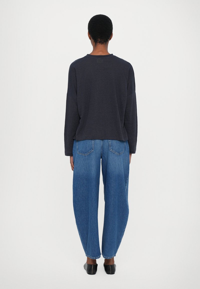 Dunkles langärmeliges Oberteil mit lockerer Passform, kombiniert mit hellblauen hochgeschnittenen weiten Jeans und schwarzen flachen Schuhen. Einfaches Design, keine Muster.