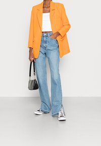 Orange oversized blazer, white cropped top, light blue flared jeans, black and white sneakers, mini black handbag with a textured finish.