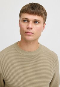 Beige geribbelde gebreide trui met een ronde hals, voorzien van textuurstof en een aansluitende pasvorm. Subtiel ontwerp zonder zichtbare logo's.