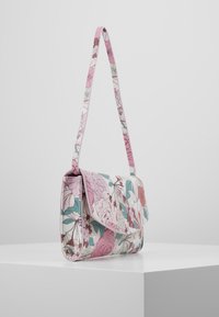 Floral print handbag with a pink strap and accents, featuring a fold-over design and glossy texture, displayed on a white pedestal.