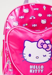 Rózsaszín Hello Kitty hátizsák fényes felülettel, szív alakú mintával, fehér macska grafikával és színes édesség- és szivárvány mintákkal.