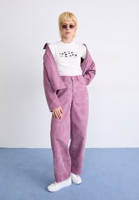 Pink, cropped denim jacket and matching high-waisted pants with a faded finish. White t-shirt features a black graphic print. White sneakers.