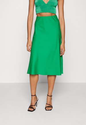 Falda midi de satén verde con una textura suave, que presenta un dobladillo acampanado y una cintura elástica. Combinada con tacones negros de tiras.
