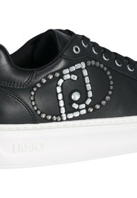 Sneaker in pelle nera con suola in gomma bianca, caratterizzata da un motivo decorativo di pietre argento e trasparenti lungo il lato. Logo visibile.