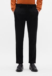 Čierne, presne strihané nohavice so slim fit, ktoré majú bočné vrecká, hladkú textúru a opasok na pása. V kombinácii s čiernymi topánkami.