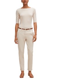 Pruhovaná, světle béžová blůza s tříčtvrtečními rukávy je doplněna krémovými kalhotami. Hnědý kožený opasek a světlé nazouvací boty dokončují outfit.