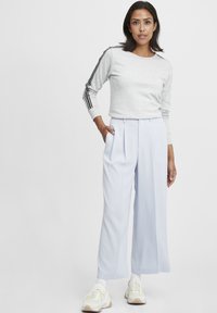 Felpa grigia chiara con strisce laterali nere, abbinata a pantaloni a gamba larga blu pastello e sneakers beige con dettagli gialli.