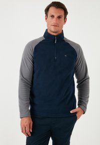 Fleece pullover features a navy body and gray sleeves, half-zip neck, soft texture, and a small logo near the chest.