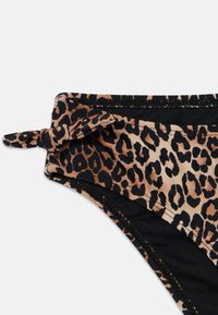 Bikini apakšda ar leoparda rakstu, kurai ir mezgla detaļa jostasvietā. Galvenokārt brūngana un melna krāsa ar gludu, stiepjamā auduma. 
