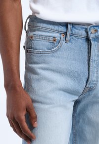 Jeans de mezclilla azul claro con corte ajustado, que cuentan con herrajes en tono cobre, cinco bolsillos y detalles de costura visibles.