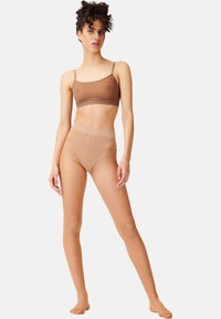 Bralette marrone leggero e collant modellanti a vita alta, entrambi trasparenti con una texture liscia, che si abbinano al tono della pelle e offrono un aspetto senza interruzioni.