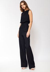 Czarny kombinezon bez rękawów z szerokimi nogawkami, z dopasowanym paskiem w talii i prostymi liniami. Gładka faktura i minimalistyczny design.