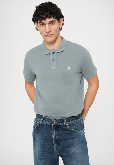 Γκρι πόλο πουκάμισο από μαλακό υλικό, με γιακά, τρία κουμπιά και κεντημένο λογότυπο στο στήθος, σε συνδυασμό με μπλε τζιν.