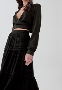 Top nero a maniche lunghe corta con scollo a V profondo abbinato a una gonna nera a balze, lunga fino alla caviglia, realizzata in tessuto morbido e dalla trama delicata.