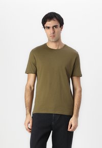 Camiseta de algodón verde oliva con cuello redondo y mangas cortas, que presenta una textura suave y un diseño sencillo y clásico.