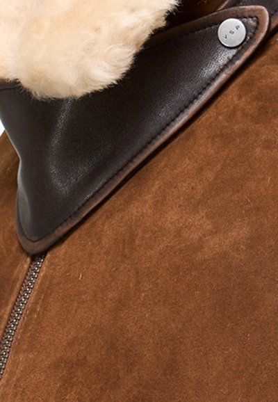 Giacca in suede marrone con colletto in pelle scura, caratterizzata da un dettaglio con bottone argentato e un morbido interno in shearling testurizzato. Chiusura frontale con cerniera.