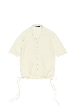 Camisa de manga corta color crema, hecha de una tela ligera, con un cierre de botones en la parte delantera, dobladillo ajustable con cordón y un corte holgado. Presenta un cuello con solapa.