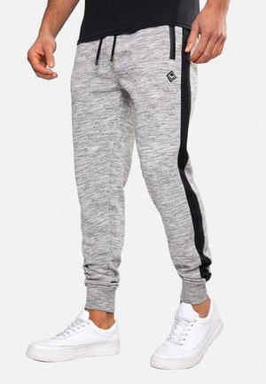 Gray melange joggers with black side stripes, elastic waistband with drawstring, tapered fit, and ribbed cuffs. Worn with white sneakers.