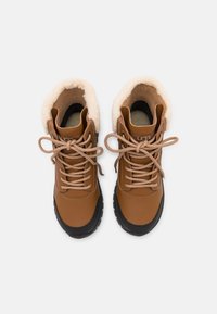 Botas de cuero marrón hasta el tobillo con un suave forro de fleece color crema, punta redonda y suela de goma negra. Presentan cordones y costuras beige.