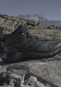 Sort Adidas Terrex vandresko med Gore-Tex, vist på klippefyldt terræn mod en sløret bjergbaggrund.