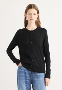 Svart cardigan med rund hals, lange ermer og knaplukking. Laget av et mykt materiale, med en løsning passform og ribbede mansjetter.
