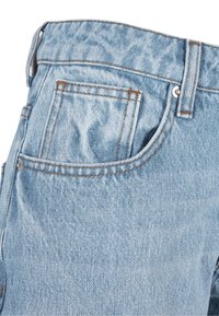 Jean en denim bleu clair en gros plan montrant la poche arrière, la boucle de ceinture et les détails des coutures à rivets.