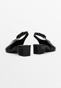 Tacchi slingback in pelle nera con punta arrotondata, piccolo tacco a blocco e cinturino alla caviglia regolabile. Texture liscia con design minimalista.