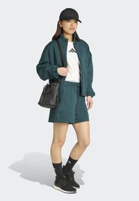 Teal athletic jacket and shorts in soft fabric, paired with a white t-shirt and black cap. Accessories include a black sling bag and black sneakers.