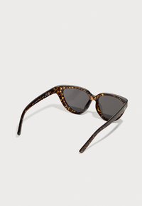 Tortoiseshell sunglasses with an angular cat-eye design, dark lenses, and slender arms featuring a textured pattern and brand detailing.
