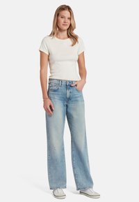Camiseta blanca de manga corta combinada con unos pantalones vaqueros de pierna ancha en un azul claro. Los jeans tienen una textura desvanecida y detalles de desgaste sutiles. Zapatillas blancas.