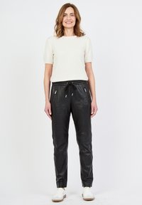 Svarta läderjoggers med dragsko i midjan, med dragkedjefickor, kombinerade med en krämfärgad stickad topp och vita sneakers. Slät textur.