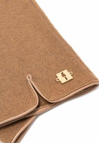 Brązowa wełniana tkanina o fakturowanym wykończeniu, z beżową skórzaną lamówką i złotym metalowym logo. Zbliżenie podkreśla szwy.