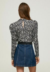 Blusa floreale a maniche lunghe con spalle imbottite, con motivo nero, grigio e bianco; apertura a chiave sul retro. Abbinata a una gonna di jeans a vita alta.