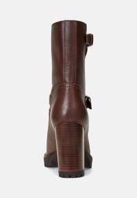 Brązowy skórzany botek za kostkę z teksturowanym wykończeniem, masywnym drewnianym obcasem, tylnym detalem z klamrą oraz smukłym, eleganckim designem.