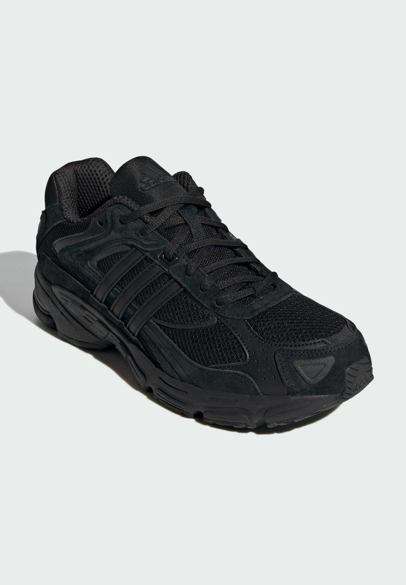 Scarpa sportiva nera con materiali in rete e suede, dotata di una suola imbottita, dettagli testurizzati e un sistema di lacci prominente.