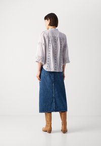 Gai pelēks blūze ar mežģīņu detaļām, trīs ceturtdaļu garuma piedurknēm un augstu apkakli, apvienota ar garu džinsu svārku un augstiem brūniem zābakiem.