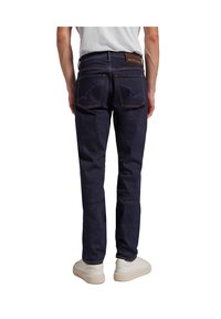 Dunkelblaue Denim-Jeans mit schlanker Passform, ausgestattet mit Gesäßtaschen, einem braunen Lederpatch und Kontrastnähten. Niedriger Bund.