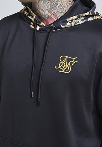 Sudadera negra para hombres con logo dorado, con forro de capucha estampado, cierre de cordón y textura suave.