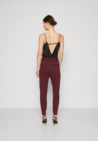 Black sleeveless top with a polka dot pattern and open back, paired with maroon fitted trousers and black stiletto heels.