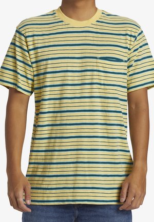 Person iført en gul og blå stribet T-shirt med korte ærmer og en brystlomme samt blå jeans, vist fra nakke til hofter.