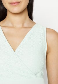 Vestido verde menta com uma textura de renda, decote em V profundo e alças largas. Corpete suave com cintura ajustada.
