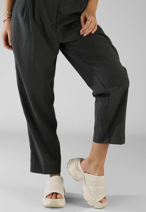 Sandali beige senza lacci con tomaia perforata e suola in gomma spessa, abbinati a pantaloni cropped larghi di colore grigio scuro.
