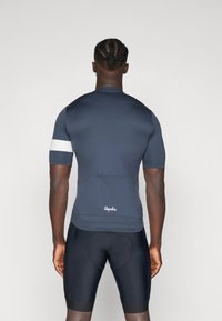 Kurzarm-Radtrikot aus dunkelblauem Stoff mit weißem Akzentband am Arm. Verfügt über eine rückseitige Tasche und ein Logo an der Taille. Figurbetonter Schnitt.