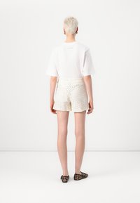 White cotton t-shirt with a green logo on the back, paired with cream shorts featuring intricate lace patterns. Worn with leopard print flats.
