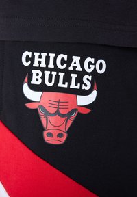Fekete textília, amelyen egy nagy piros és fekete bika grafikája látható, fehér felirattal, amelyen a „CHICAGO BULLS” szöveg olvasható, mindez piros és fehér háromszög alakú díszítéssel a háttérben.