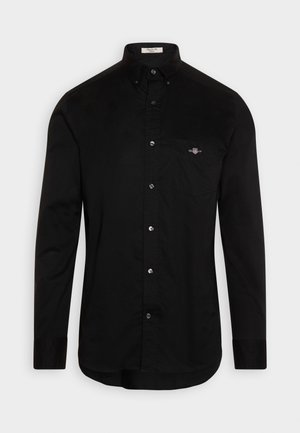 Camisa negra de botones, hecha de algodón, con cuello puntiagudo, mangas largas y un bolsillo en el pecho con un pequeño logo bordado en color.