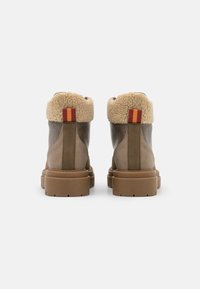 Stivali alla caviglia in pelle marrone con colletto in shearling, tessuto testurizzato e suola in gomma spessa. Presentano un dettaglio a strisce rosse e gialle sul retro.